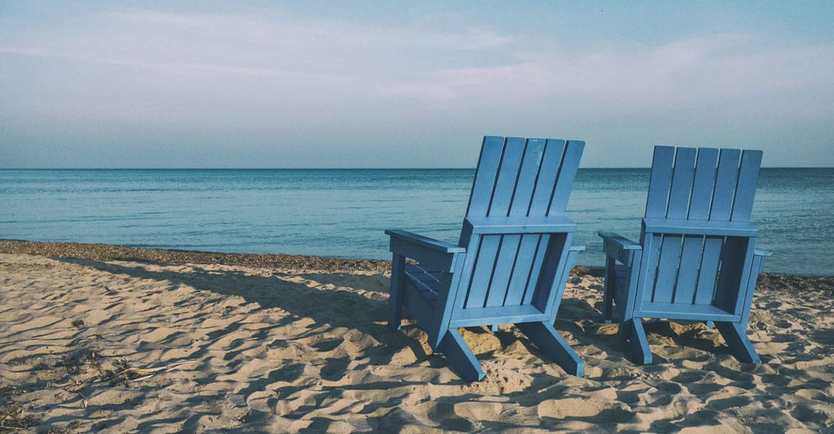 a couple of lawn chairs sitting on top of a sandy beach